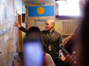 Guide at the Fox Theater looks up and touches a wall of signatures as students look on 